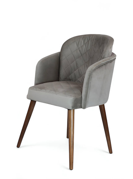 Front angled view of the Vaya Home Silver dining chair with gray upholstery, diamond-quilted backrest, curved arms, and tapered wood legs.