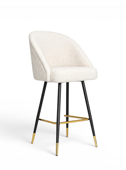 Front angled view of the Vaya Home Sloan bar stool with white upholstery, a curved backrest, black metal legs, and gold footrest detailing.