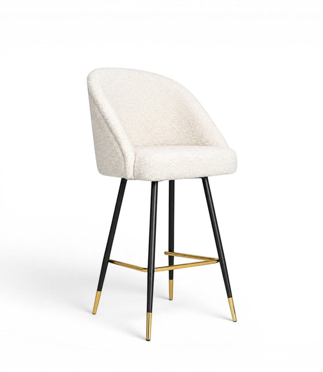 Front angled view of the Vaya Home Sloan bar stool with white upholstery, a curved backrest, black metal legs, and gold footrest detailing.