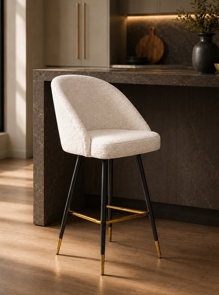 Vaya Home Sloan bar stool with white upholstery, black metal legs, and gold footrest detailing, styled at a modern kitchen island.