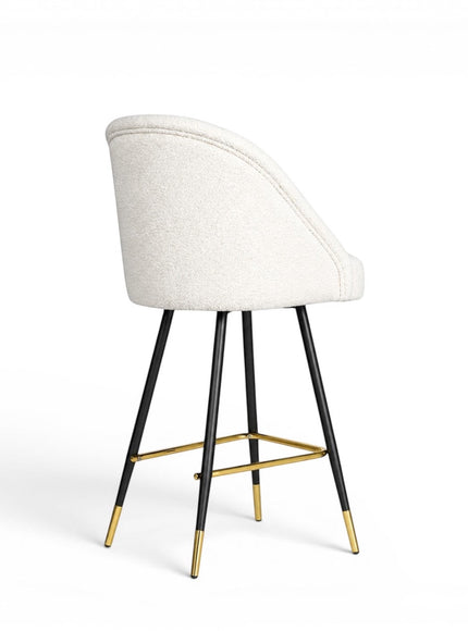 Rear angled view of the Vaya Home Sloan bar stool featuring white upholstery, a curved backrest, black metal legs, and gold footrest detailing.
