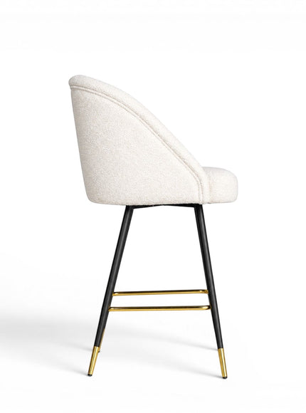 Side view of the Vaya Home Sloan bar stool with white upholstery, a curved backrest, black metal legs, and gold footrest detailing.
