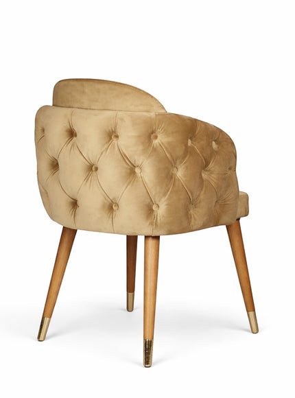 Rear angled view of the Vaya Home Sorelle dining chair with diamond-tufted beige velvet outer back and tapered legs with gold caps.