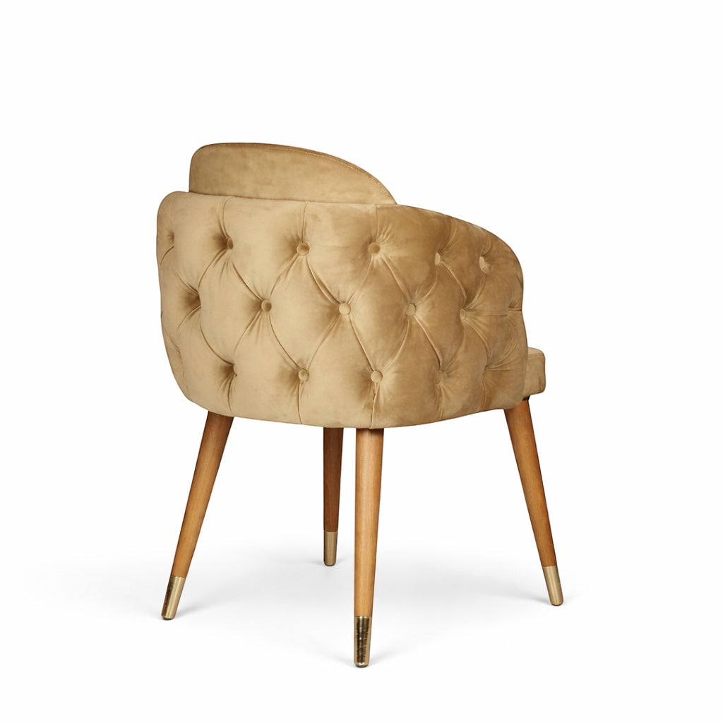 Rear angled view of the Vaya Home Sorelle dining chair with diamond-tufted beige velvet outer back and tapered legs with gold caps.