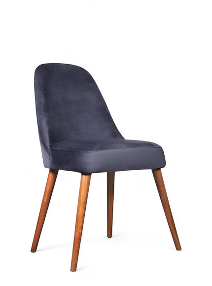Front angled view of the Vaya Home Stretto dining chair with dark blue velvet upholstery and tapered wood legs.