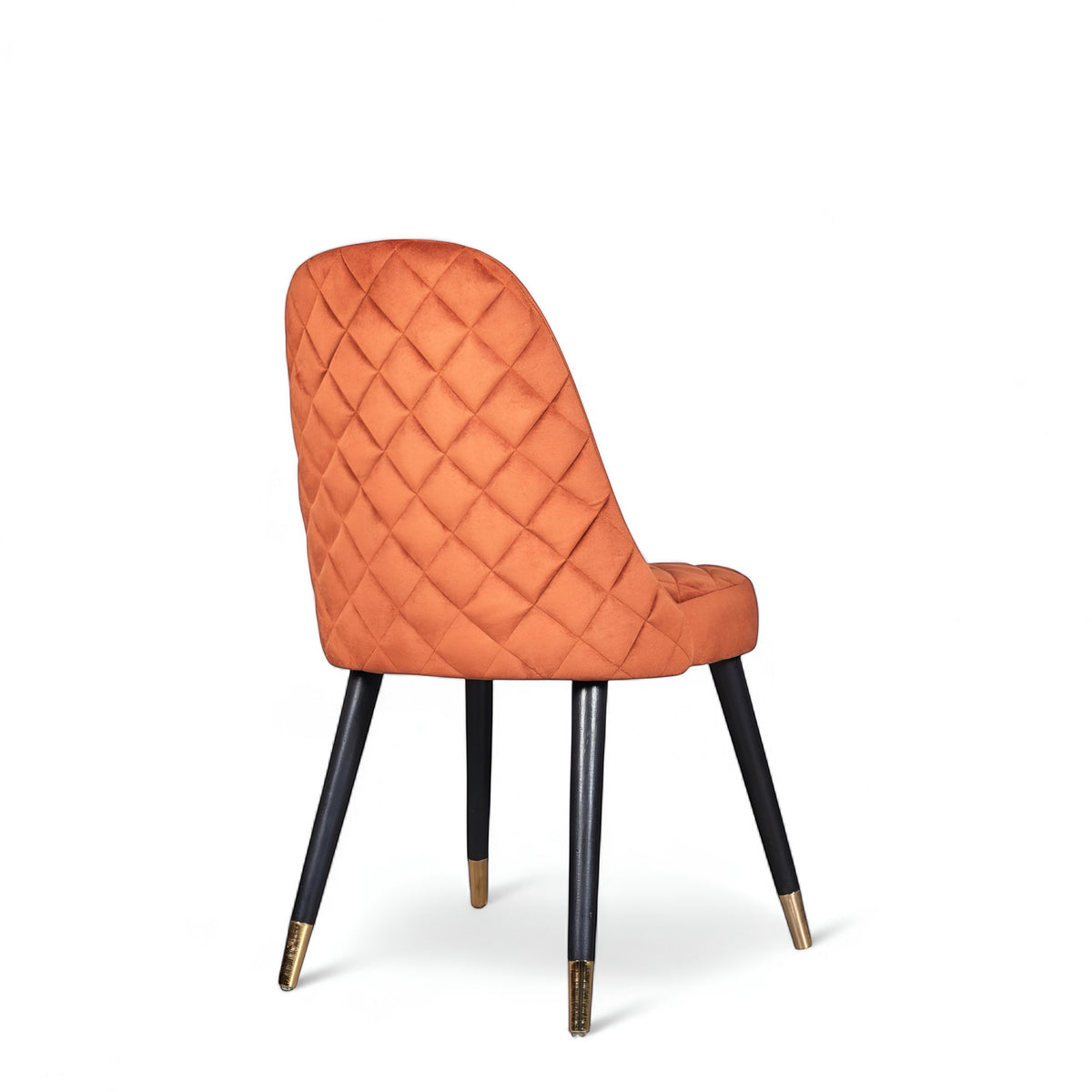 Rear angled view of the Vaya Home Stretto dining chair featuring orange velvet upholstery, diamond-quilted back detail, and black tapered legs with gold caps.