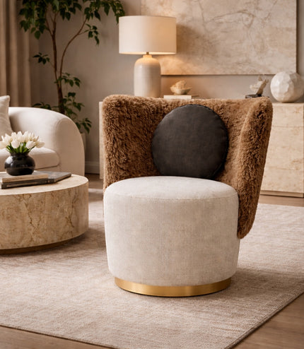 Vaya Home Valmont accent chair with a cream upholstered seat, brown textured wraparound back, gold base detail, and black round cushion, styled in a modern interior.