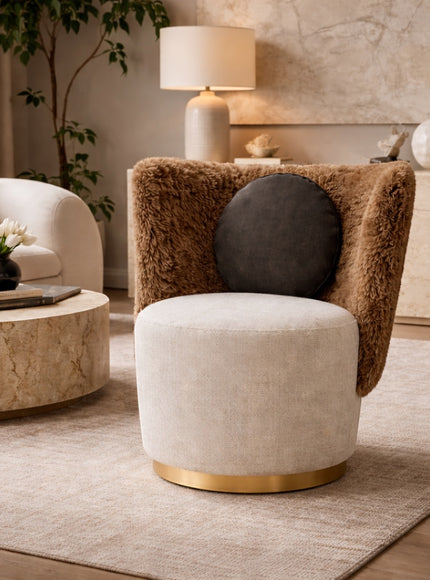 Vaya Home Valmont accent chair with a cream upholstered seat, brown textured wraparound back, gold base detail, and black round cushion, styled in a modern interior.